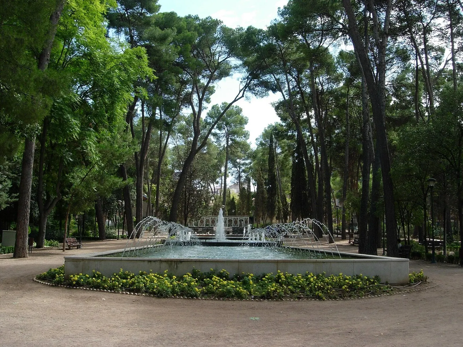 La Fuente Larga del parque Abelardo Sánchez, con chorros en arco y flores, bajo pinos altos
