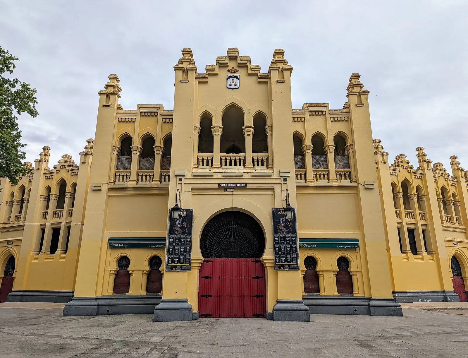 Fachada neomudéjar amarilla de la plaza de toros de Albacete, con su gran puerta roja de entrada