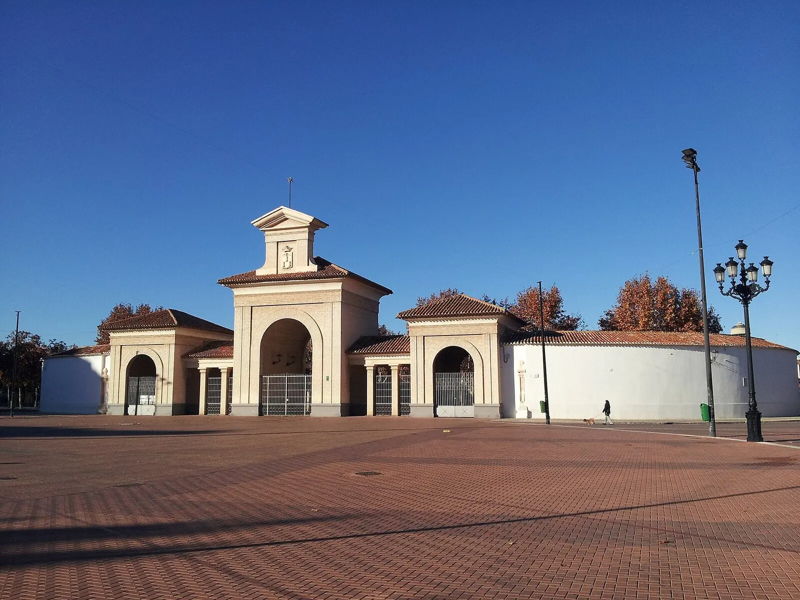 La Puerta de Hierros del recinto ferial de Albacete, de arcos blancos, ante una explanada de ladrillo vacía