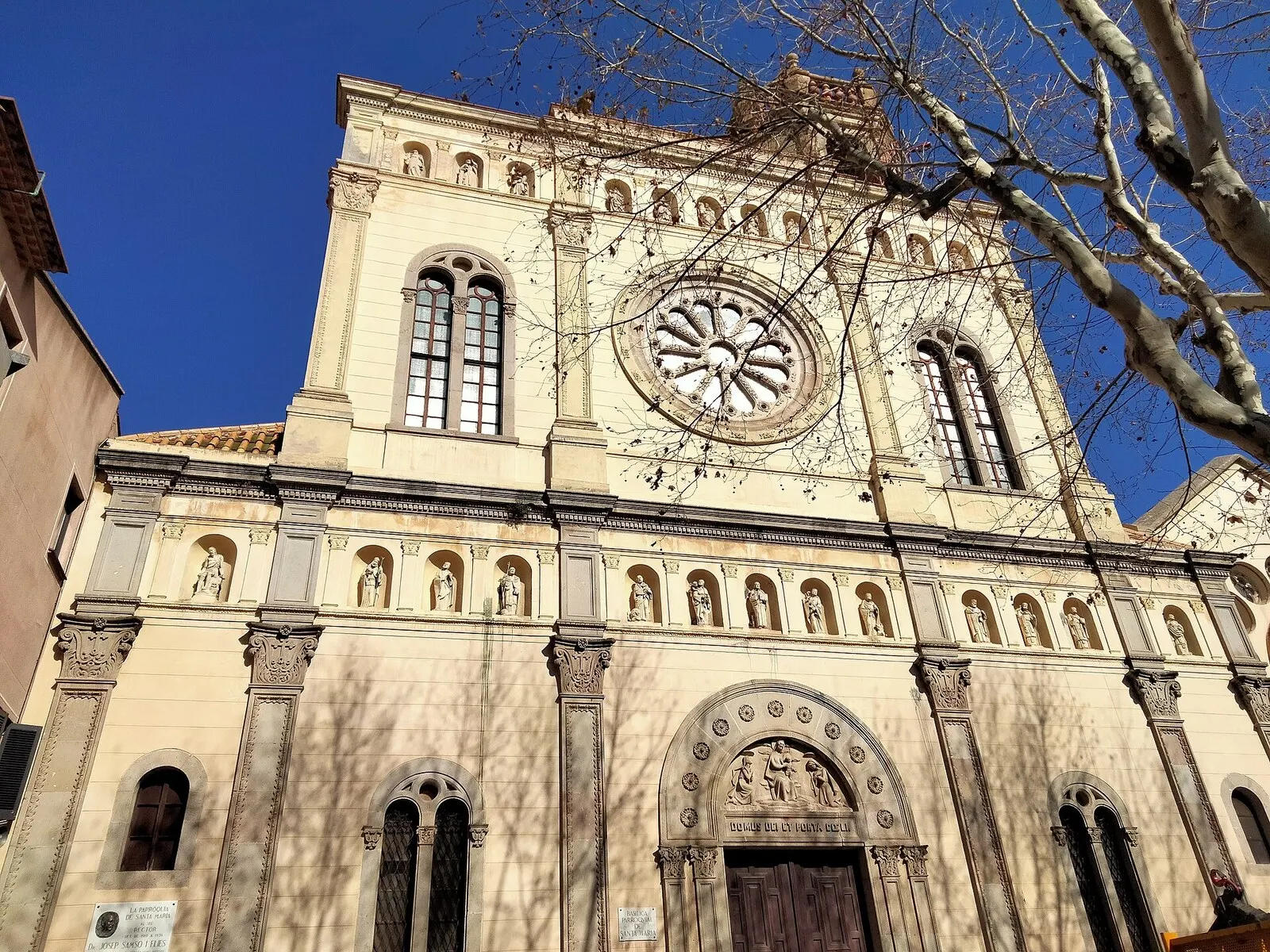 La fachada de la basílica de Santa Maria de Mataró, con su rosetón y hornacinas, bajo un cielo azul intenso