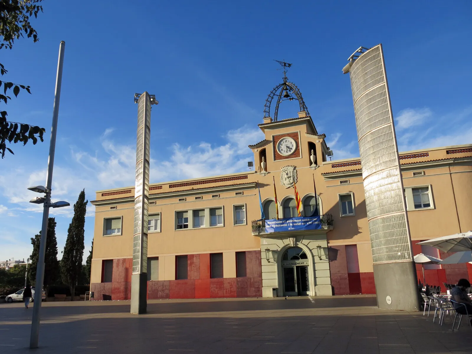 El ayuntamiento de Santa Coloma de Gramenet con su torre del reloj, entre dos columnas metálicas de la plaza