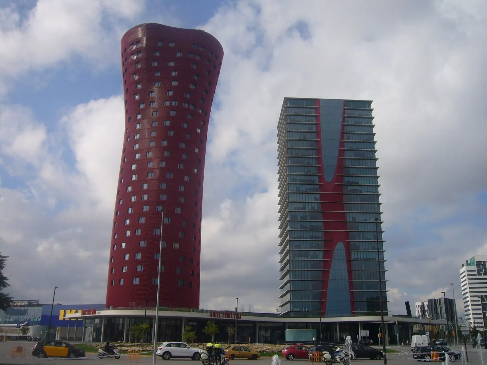 Las torres de Toyo Ito en la plaza Europa de L'Hospitalet, una roja y curvada y otra de cristal, bajo un cielo con nubes