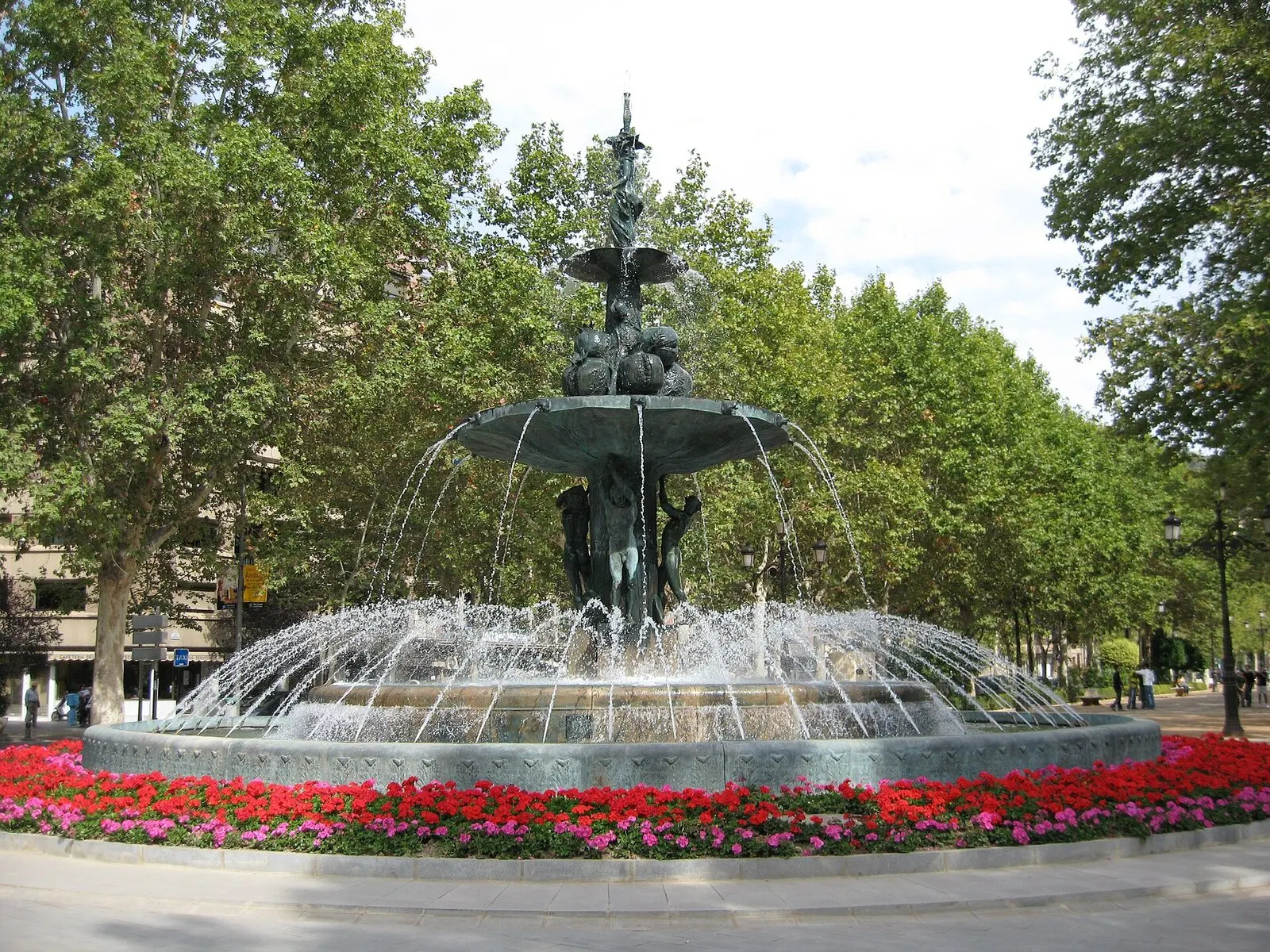 La Fuente de las Granadas, de bronce y con chorros en corona, rodeada de flores rojas en el Paseo del Salón
