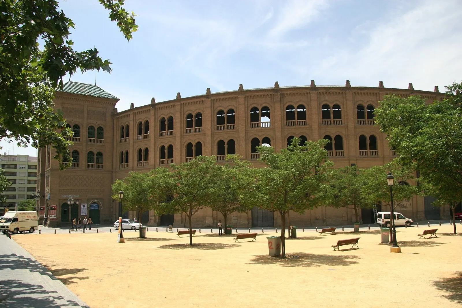 La plaza de toros neomudéjar de Granada, de ladrillo, tras una explanada de albero con árboles y bancos