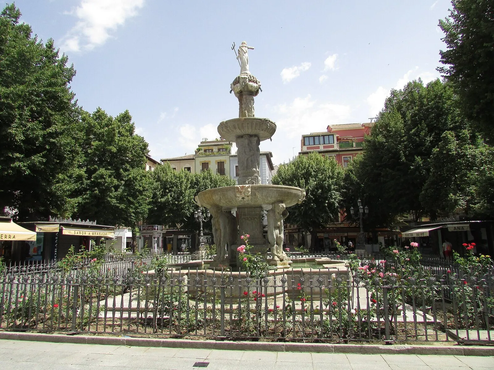 La fuente de los Gigantones en la plaza de Bib-Rambla de Granada, entre rosales y árboles, en verano