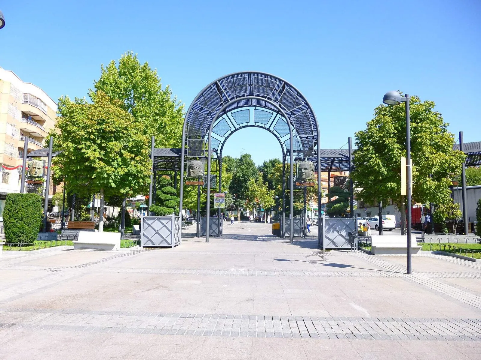 Arco metálico a la entrada del paseo arbolado de la Plaza del Pradillo, en Móstoles, en un día soleado