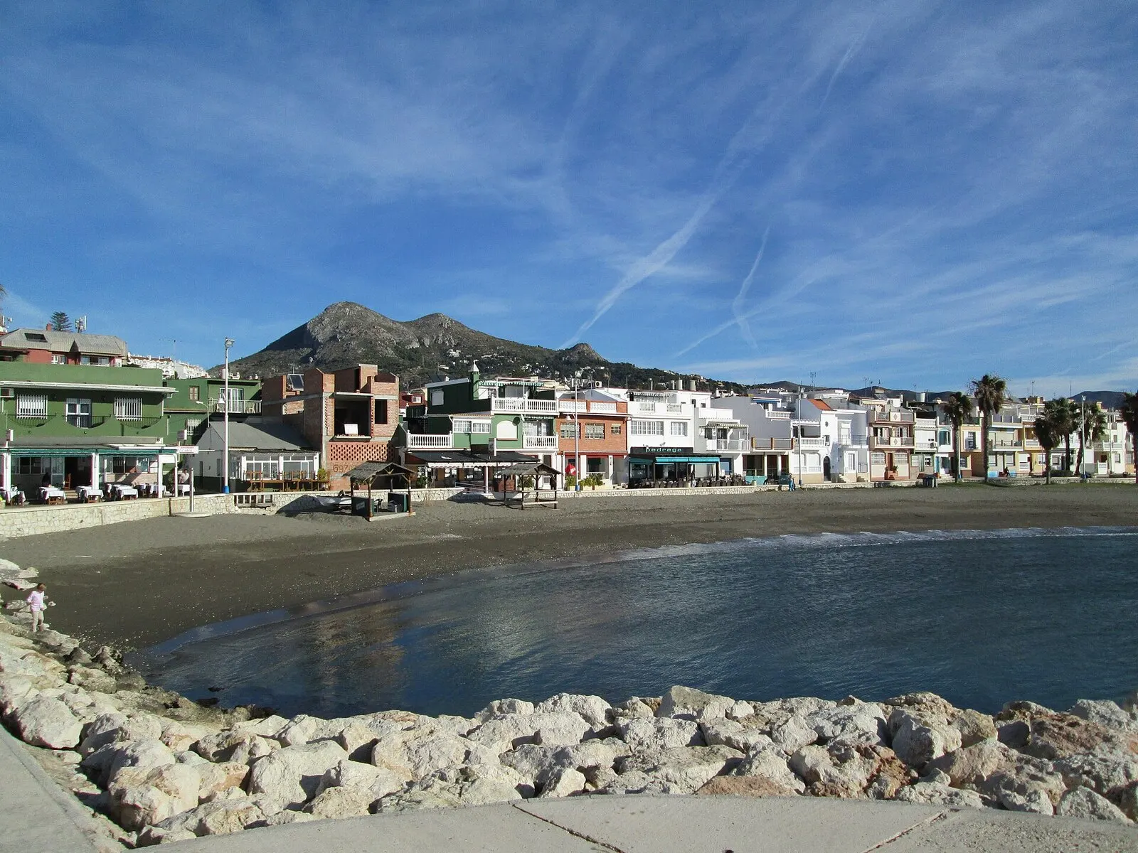 La playa de Pedregalejo con sus casas bajas de colores frente al mar y el monte San Antón al fondo