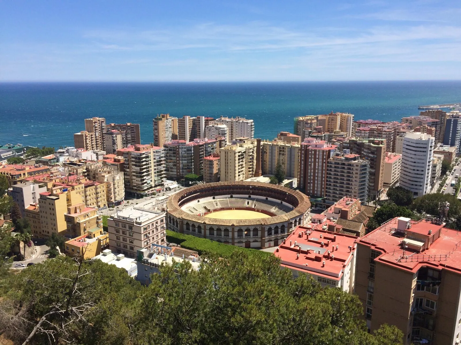 La plaza de toros de La Malagueta vista desde Gibralfaro, entre edificios, con el Mediterráneo detrás