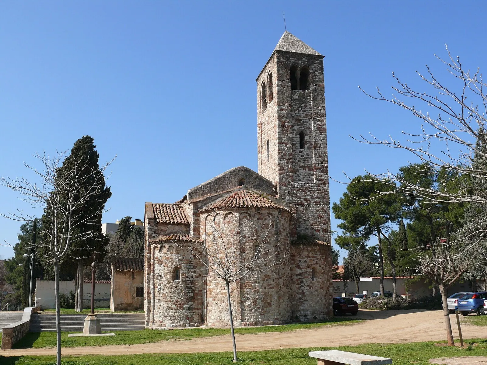 La iglesia románica de Santa Maria de Barberà, con su campanario de piedra, entre árboles y bajo un cielo azul