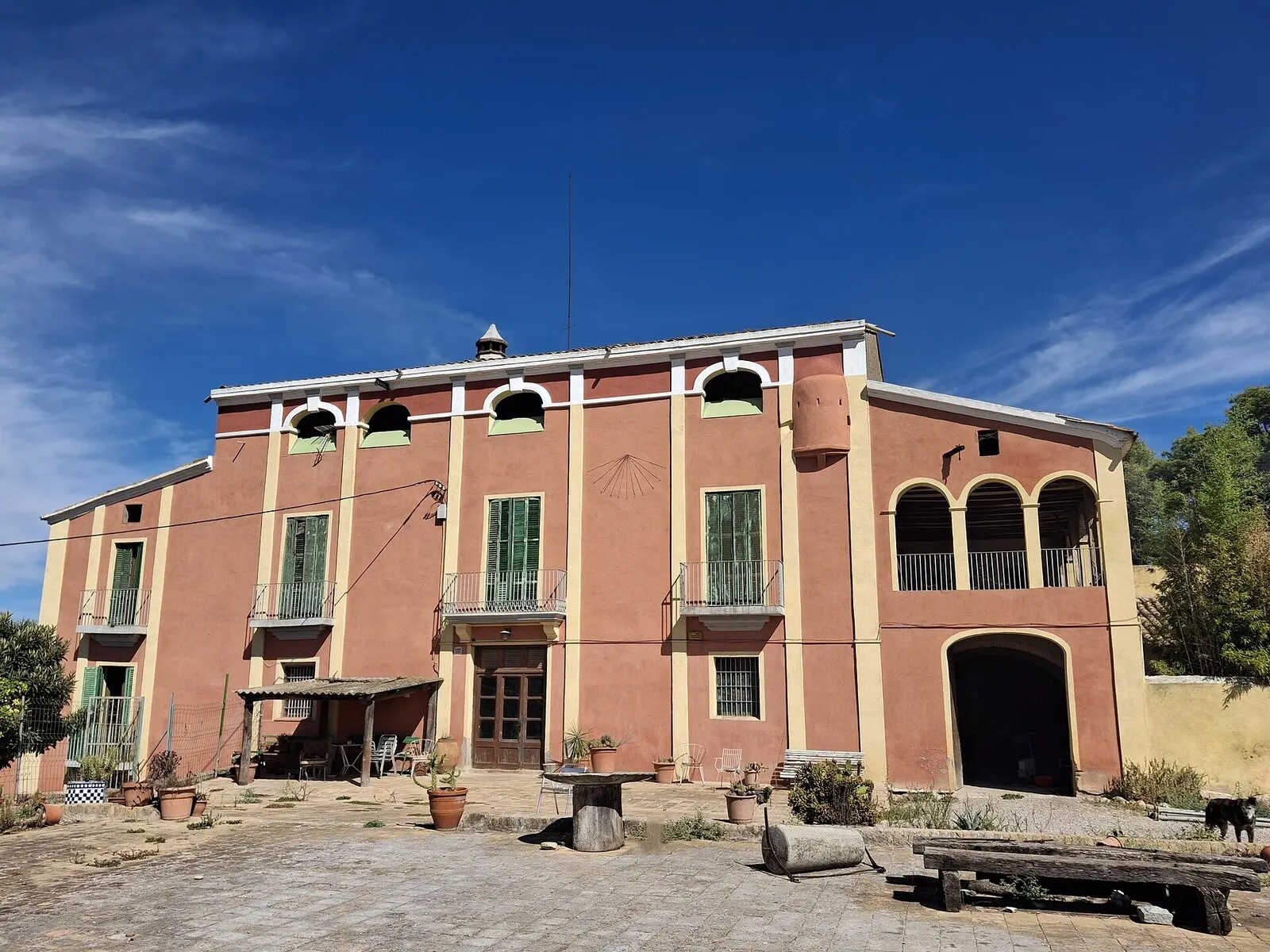 La masía de Can Corbera en Sant Quirze del Vallès, de fachada rosada con galería de arcos, bajo un cielo azul