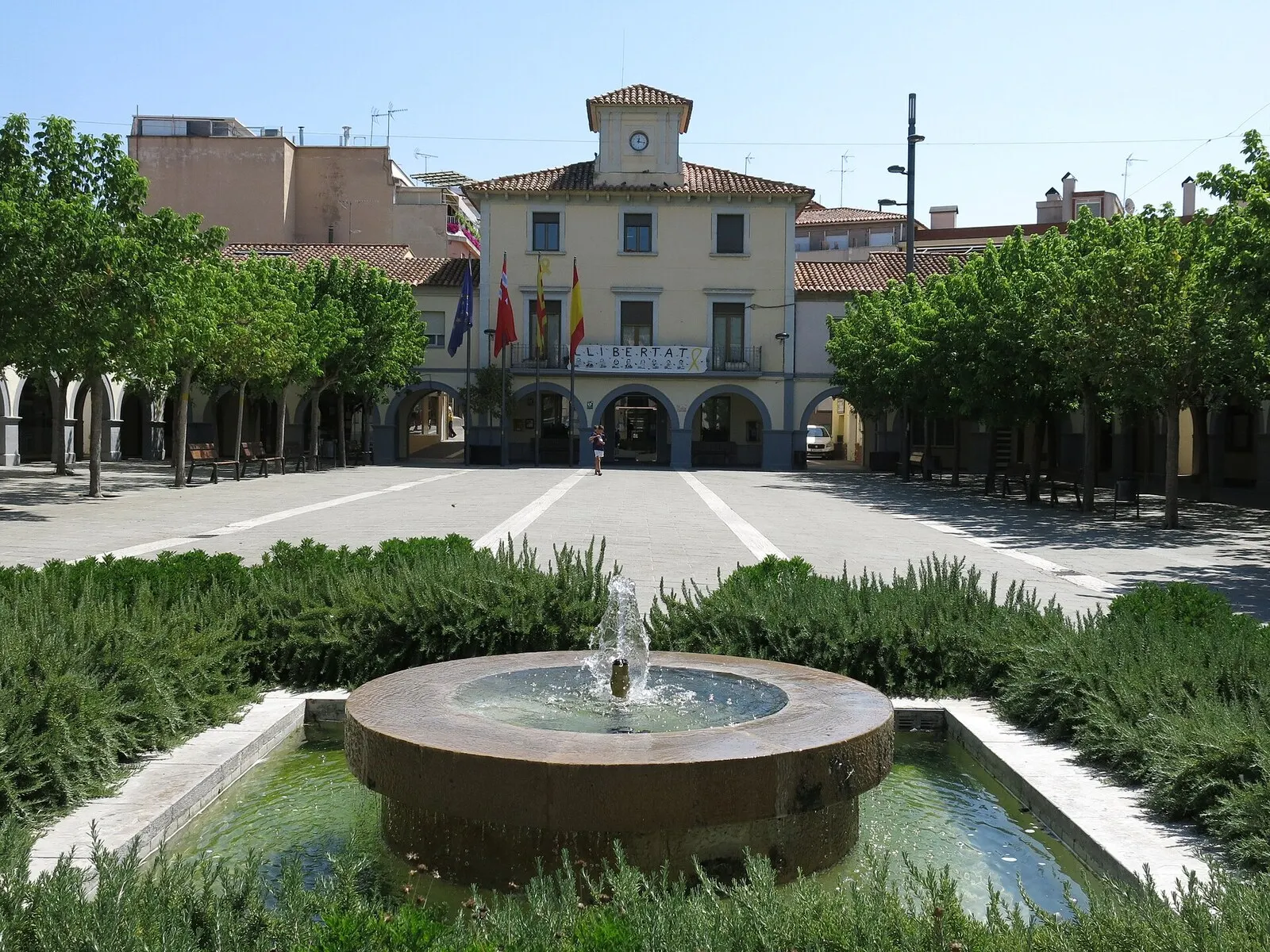 La plaza de la Vila de Sentmenat con su fuente y parterres, y el ayuntamiento porticado al fondo