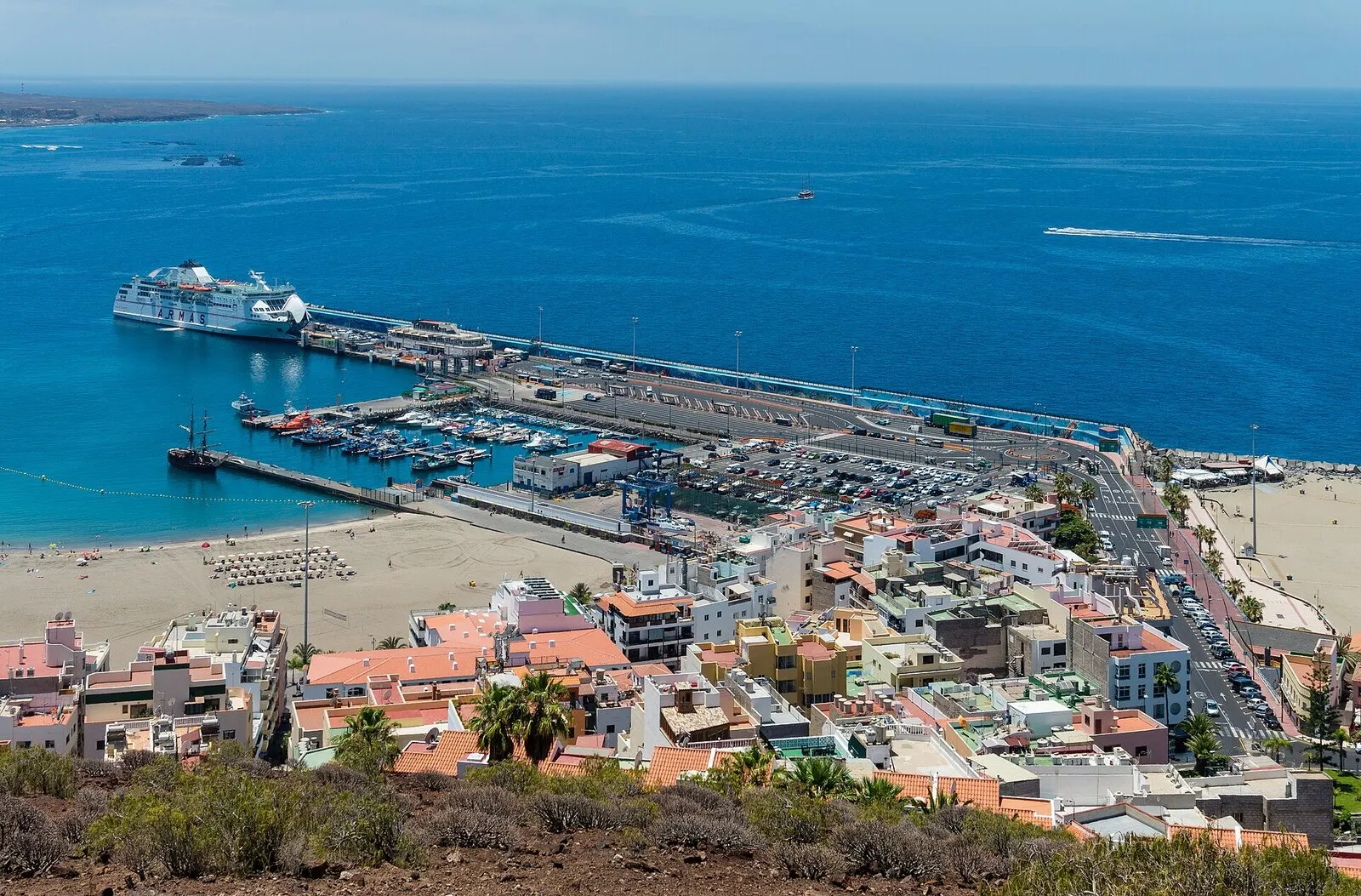El puerto y la playa de Los Cristianos vistos desde la montaña de Chayofita, con un ferri atracado y el mar azul