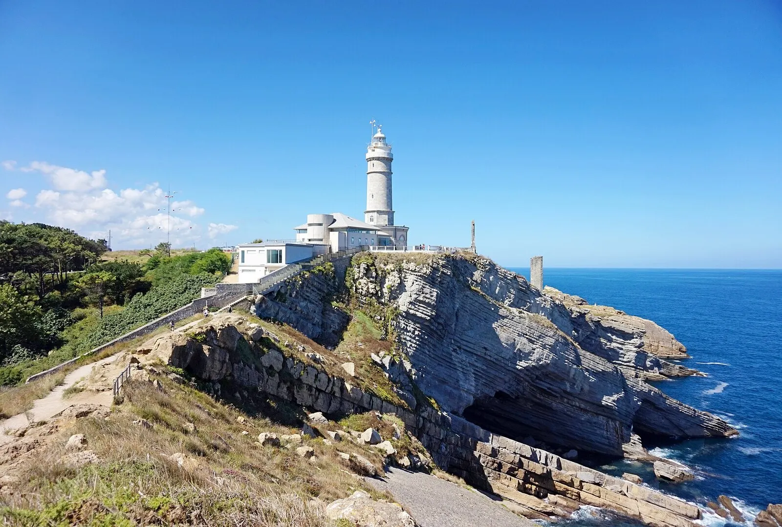 El faro de Cabo Mayor sobre un acantilado de roca estratificada junto al mar Cantábrico, en un día soleado