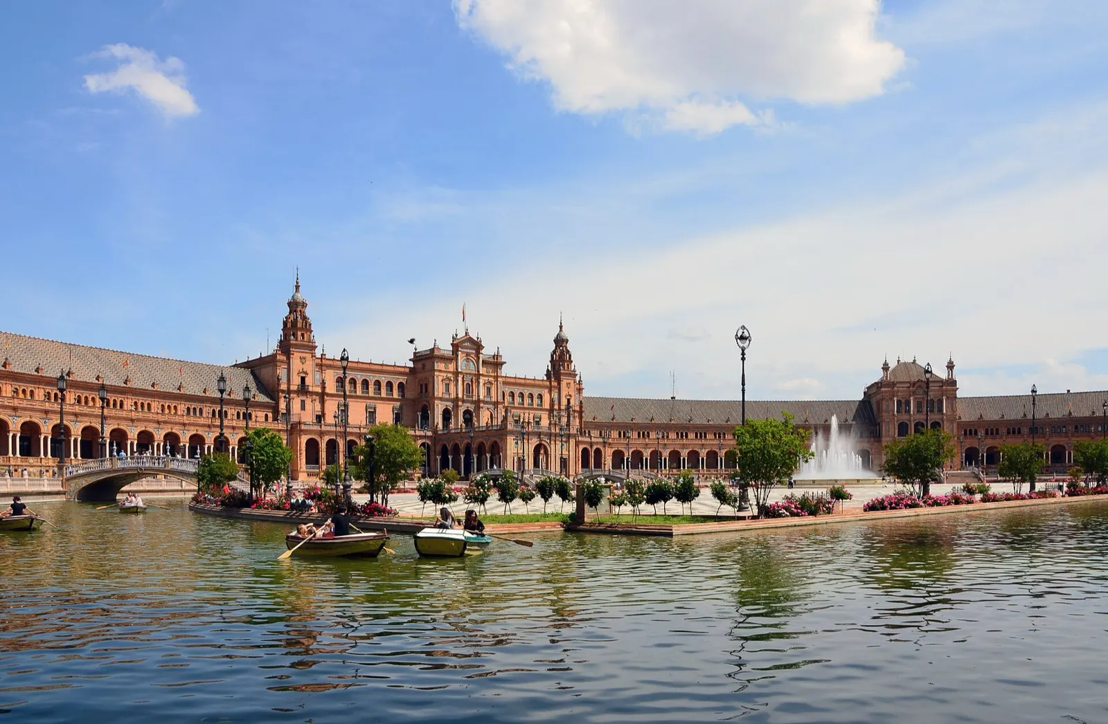 Edificio central de la plaza de España de Sevilla tras el canal, con barcas de remo y una fuente