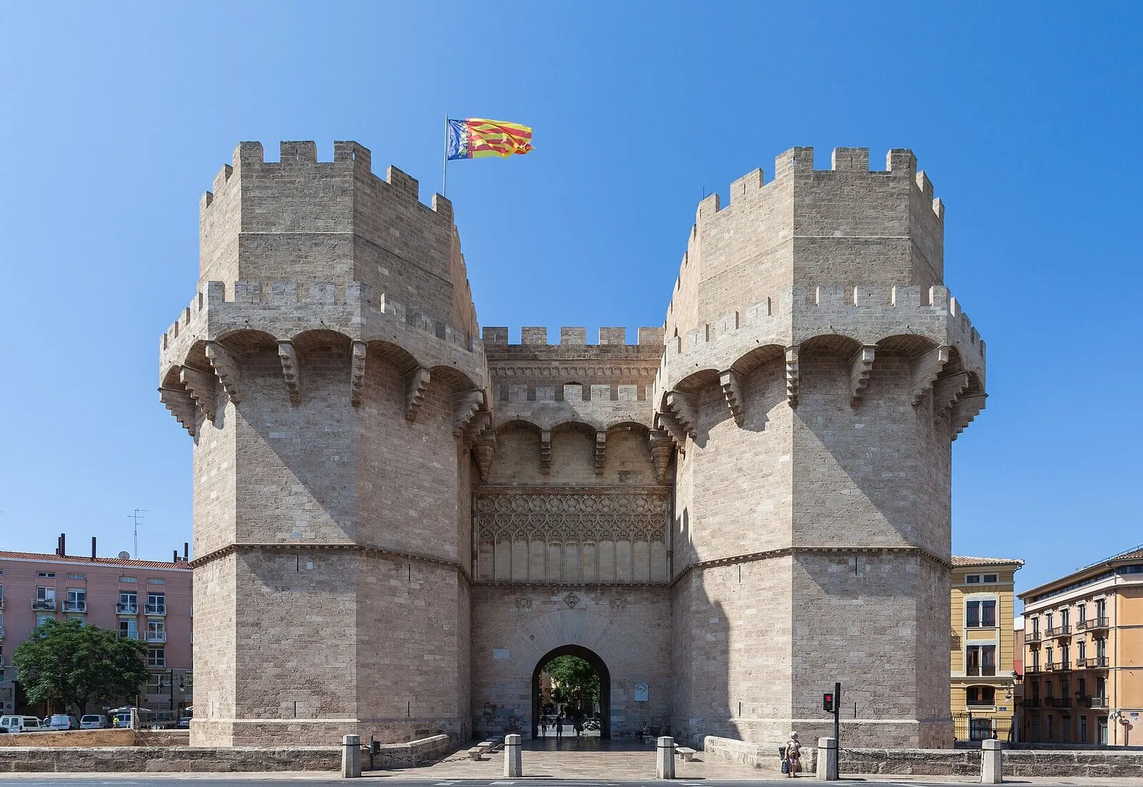 Las Torres de Serranos, puerta medieval de piedra con almenas y la senyera ondeando, bajo un cielo azul