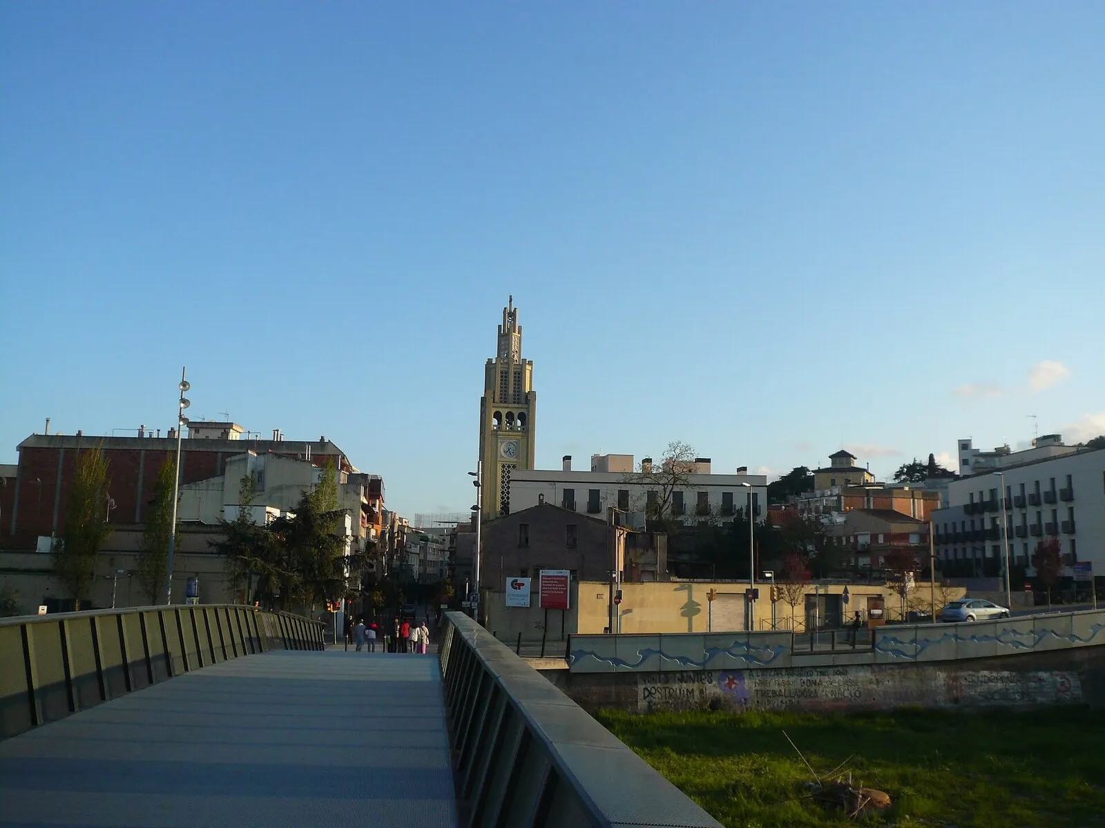 Pasarela peatonal sobre el río Ripoll hacia el centro de Montcada, con el campanario de Santa Engràcia al fondo