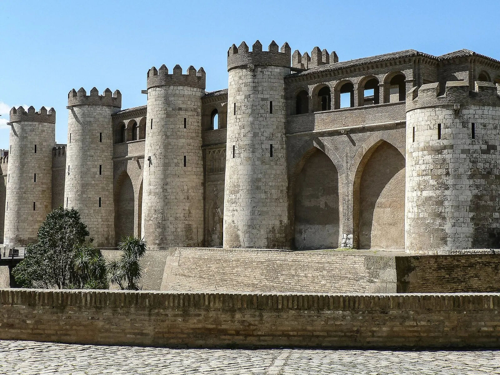 Los torreones y arcos de la muralla del palacio de la Aljafería bajo un cielo azul