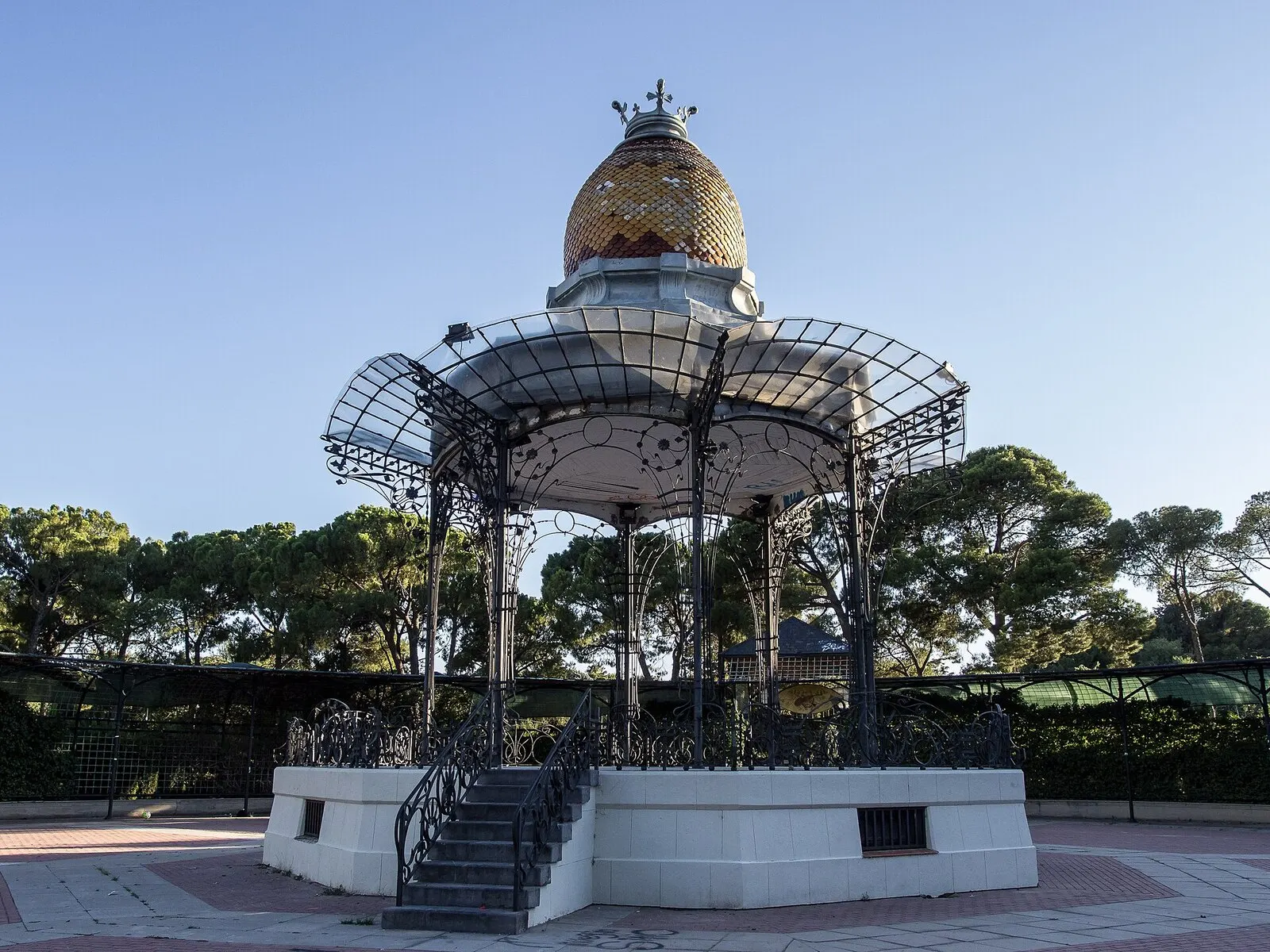 El quiosco de la música de hierro con cúpula de cerámica dorada en el parque Grande, entre pinos